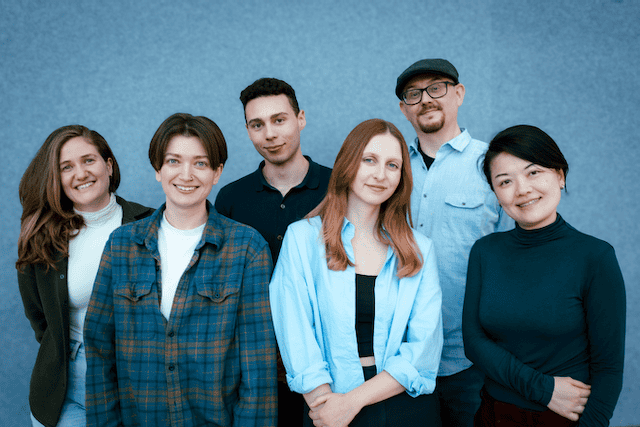 6 writers posed for a group photo against a blue background